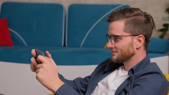 Young Man Playing Games on Phone, at Home. alt