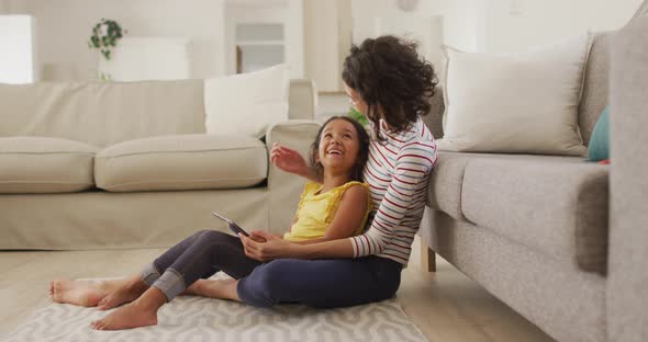 Happy hispanic mother and daughter sitting on floor using tablet alt