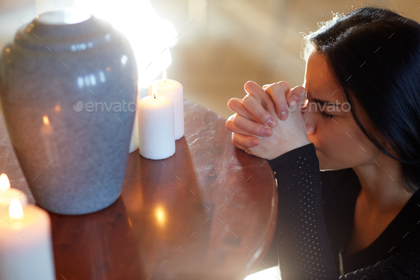 sad woman with funerary urn praying at church