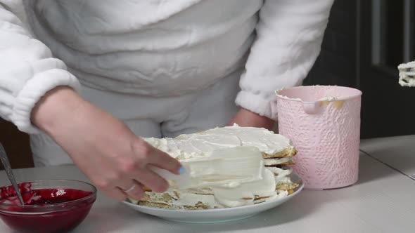 A Woman Smears A Biscuit Cake With Cream. Nearby Is A Container With Cherry Filling For The Cake alt