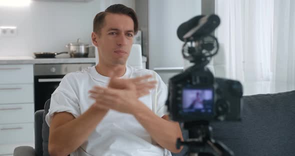 Blogger Man Filming New Vlog Video with Professional Camera Mounted on Tripod at Home While Sitting alt