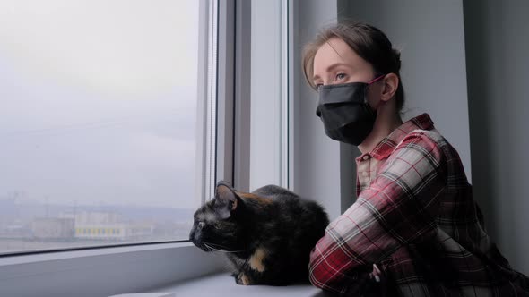 Woman in Medical Face Mask and Black Cat Looking Out of Window - Slow Motion