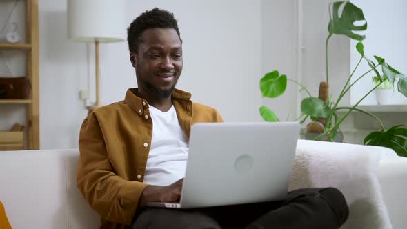 Man Using Laptop and Smiling Sitting on Couch at Home Room During Pandemic Spbas alt