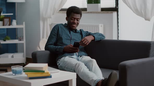 African American Man with Phone in Hands Looking at Online Streaming Services Content alt