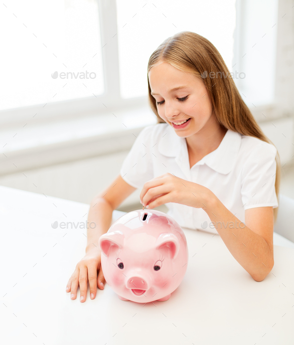 happy smiling girl putting coin into piggy bank