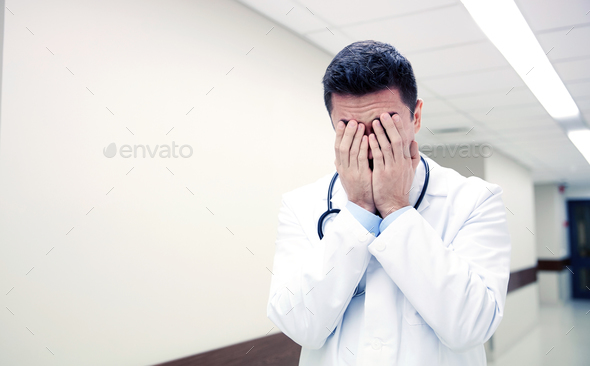 sad or crying male doctor at hospital corridor