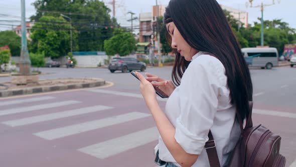 Asian backpacker woman tourist with camera stand in front of cross walk street look at mobile, alt