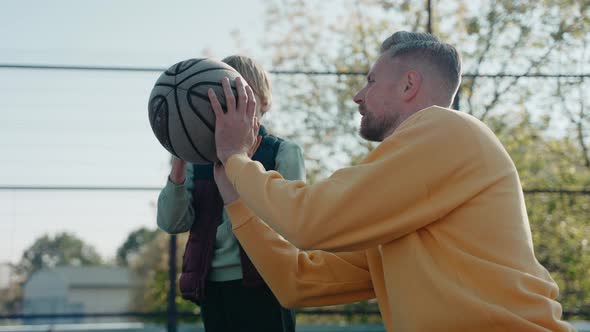 Father Teaching Son How to Hold and Throw a Basketball Ball on a Court