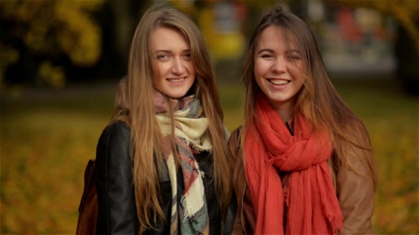 Two Smiling Young Attractive Girls with Autumn Leaves in Park at Fall Outdoors, Girlfriends Smiling