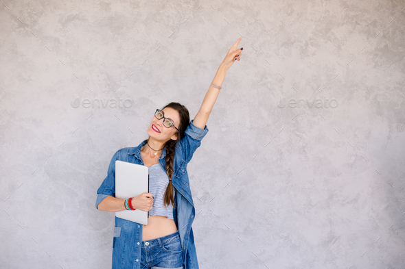 Portrait of happy girl with laptop pointing with left arm up