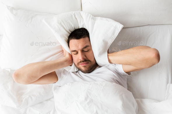 man in bed with pillow suffering from noise