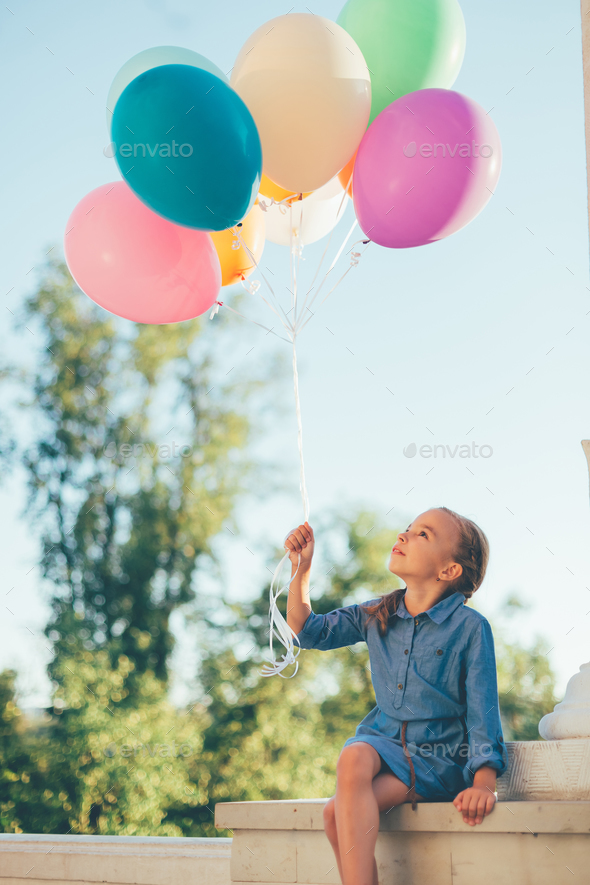 Girl holding colorful balloons looking to them while sitting in