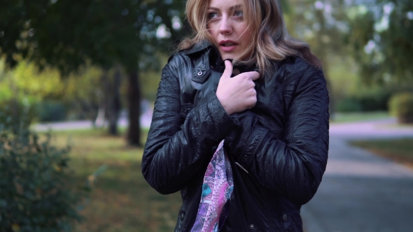 the Girl Froze in the Autumn Park. Young Woman Wrapped in a Scarf and Breathes on His Hands To Warm alt