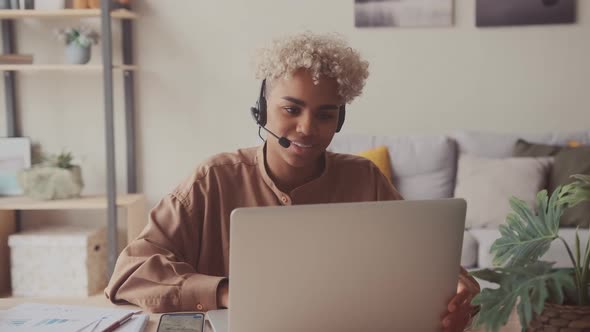 Dark Skinned Female Wears Headset Conference Video Calling in Home Office alt