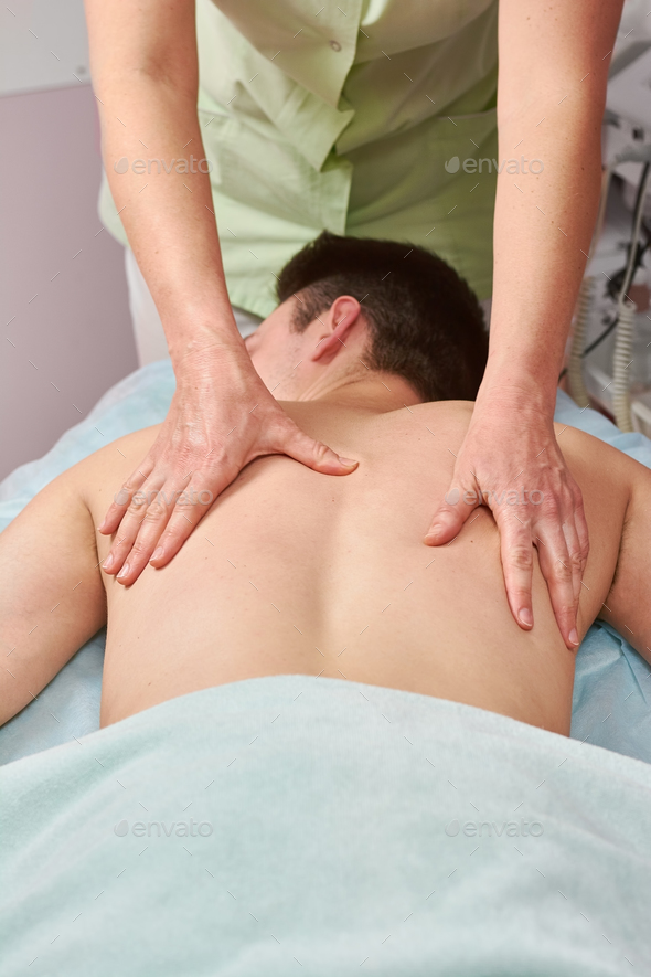 Female hands do a back massage to a man in the salon. Stock Photo by puhimec