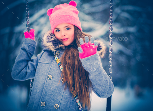 Charming little girl on swing in snowy winter - Stock Photo - Images