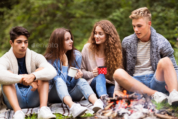 Teenagers camping in nature, sitting at bonfire.