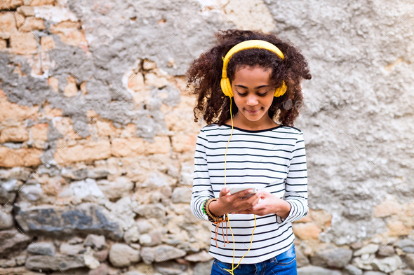 Beautiful african american girl with smart phone and earphones. - Stock Photo - Images