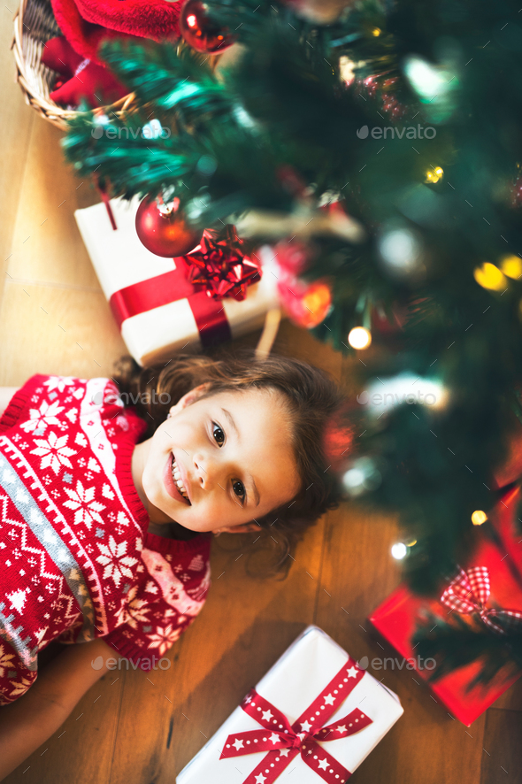 Little girl lying under Christmas tree among presents, - Stock Photo - Images