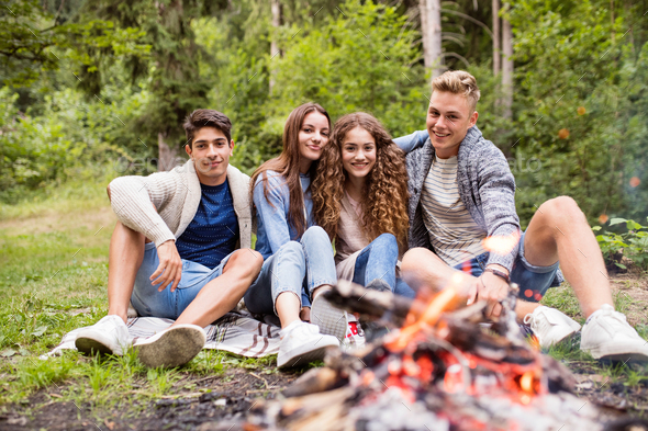 Teenagers camping in nature, sitting at bonfire.