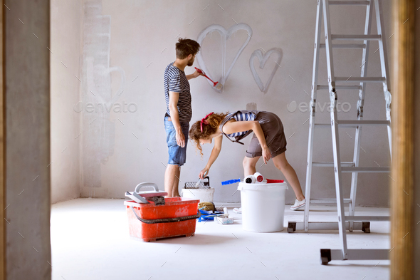 Couple painting hearts on the wall in their house.
