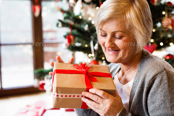 Beautiful senior woman in front of Christmas tree with present - Stock Photo - Images
