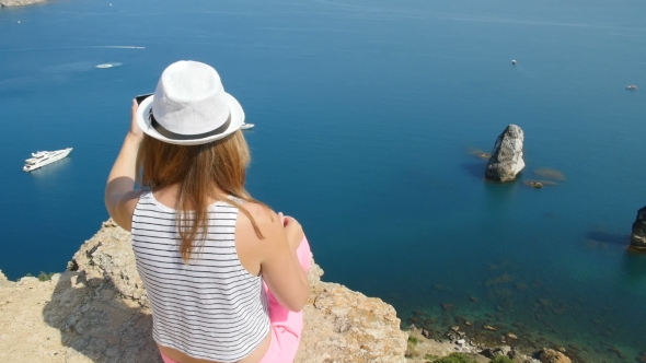 A Young Girl Does Selfie Next To the Blue Sea Sitting on a Mountain