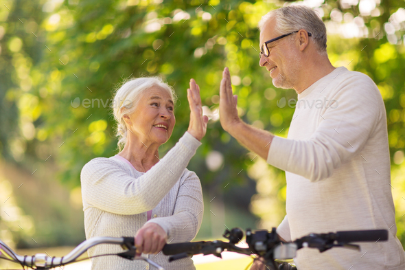 senior couple with bikes making high five at park
