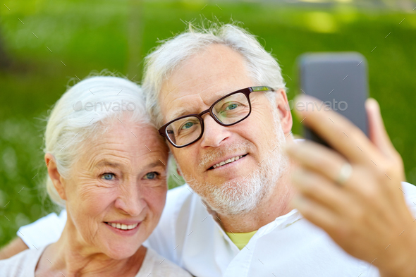 senior couple with smartphone taking selfie in summer