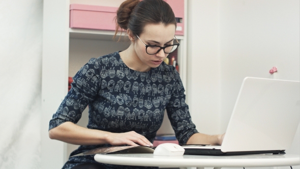 Beautiful Young Female Showroom Owner Working Using Laptop Computer and Fashion Magazine alt