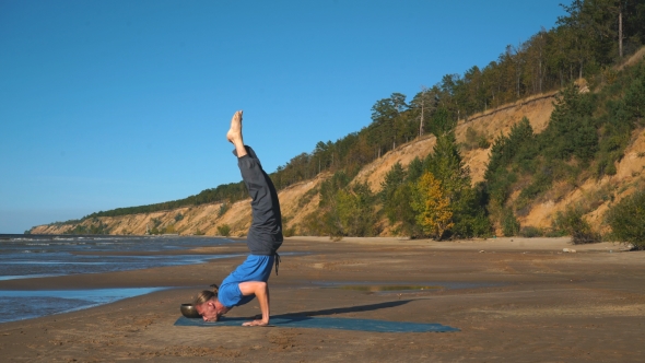 Strong Man Practicing Difficult Yoga Pose on the Beach alt