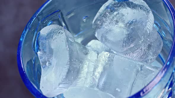 Close Up View of Empty Blue Glass in Which Cold Ice and Yellow Orange Juice Is Pouring with Smoke on