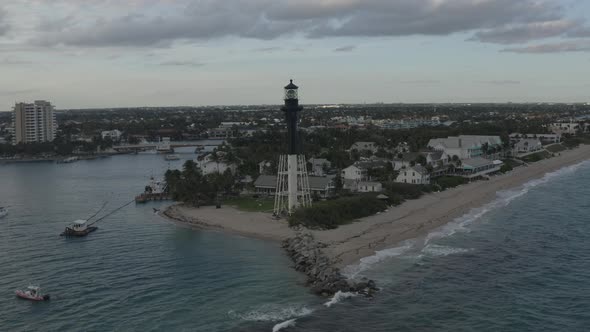 Aerial shot orbiting a lighthouse showing its surrounding bay, ocean and buildings alt