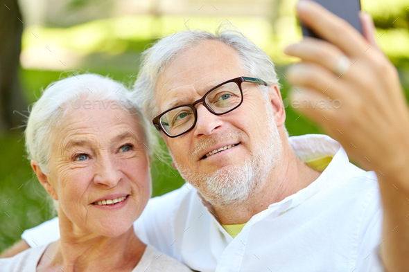 senior couple with smartphone taking selfie in summer