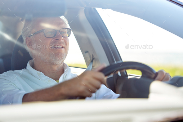 happy senior man in glasses driving car