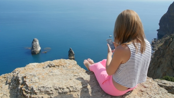 Young Girl Does Photo Near To the Blue Sea Sitting on a Mountain