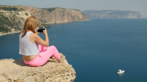 Young Girl Does Photo Near To the Blue Sea Sitting on a Mountain