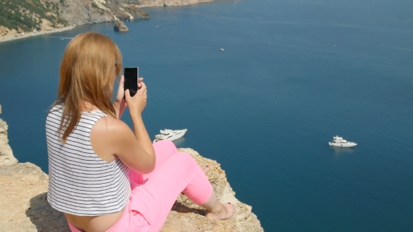 Young Girl Does Photo Near To the Blue Sea Sitting on a Mountain