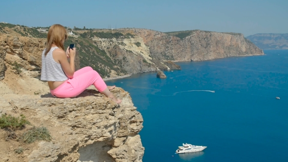 Young Girl Does Photo Near To the Blue Sea Sitting on a Mountain