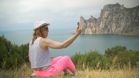 Young Girl Does Photo Near To the Blue Sea Sitting on a Mountain