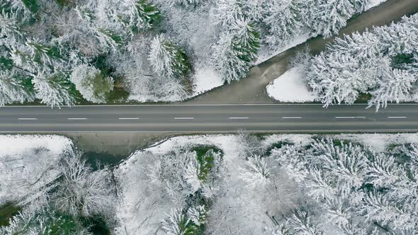 Straight from above - a fast driving car is speeding through a wintry forest landscape with top down alt