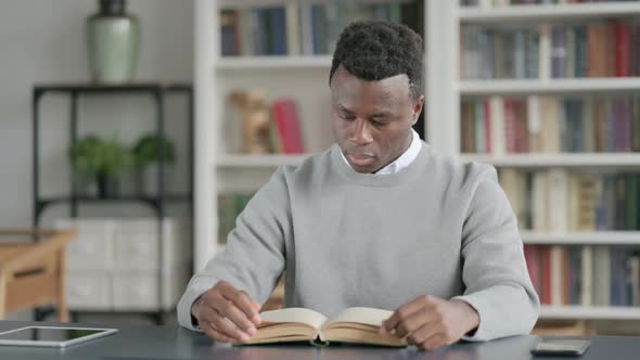 African Man Reading Book While Sitting in Library alt