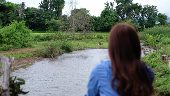 Rear view of a young woman sitting by the river in rural village