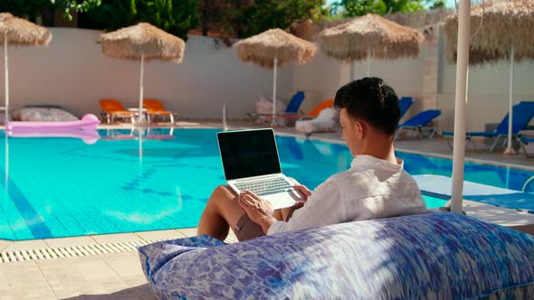 Man Talks Online By Video Call on Laptop Near Swimming Pool in Hotel on Vacation