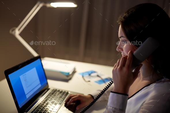 woman with laptop calling on phone at night office