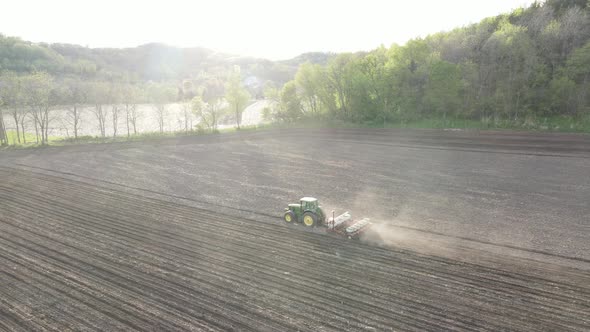 Farming working the land on a bright sunny day. View of forest filled mountain side in distance.