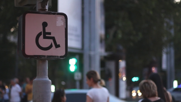 Sign of a Disabled Person Sitting on a Wheelchair Against the Background of Blurred Walking People