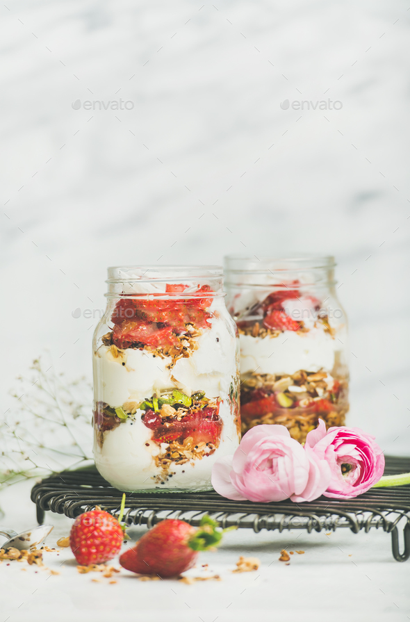 Greek yogurt, granola, fresh strawberry breakfast in jars, raninkulus flowers - Stock Photo - Images