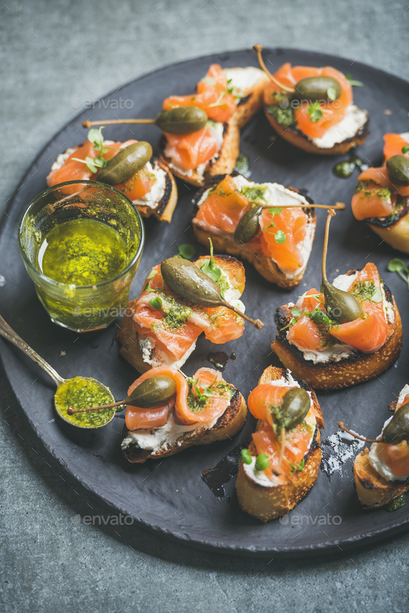 Homemade Italian salmon crostini in black plate over grey background - Stock Photo - Images