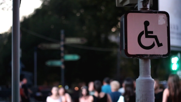 Sign of a Disabled Person Sitting on a Wheelchair Against the Background of Blurred Walking People